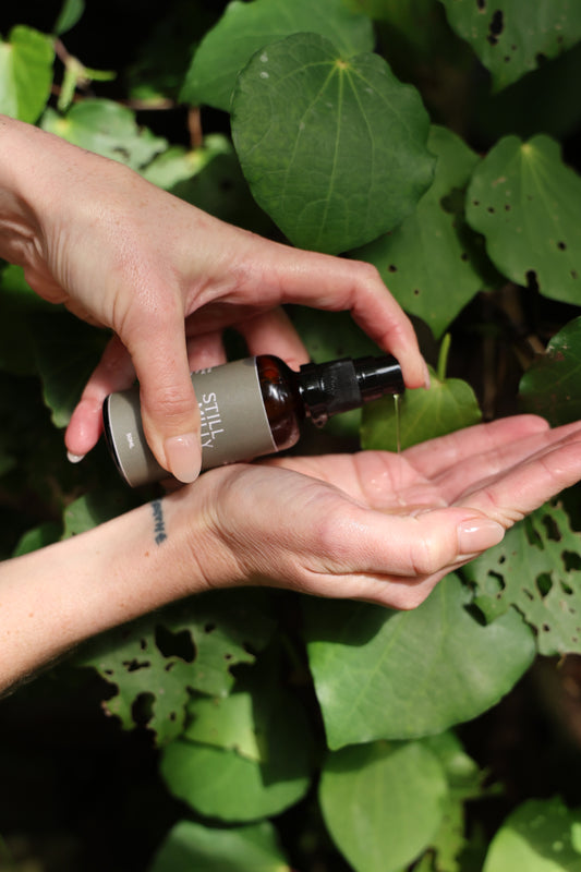 Hands dispensing Still Milly Kānuka and Mandarin Cleanser with Kawakawa in background
